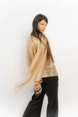 Poncho tejido de punto en color dorado con acabado brillante, diseño de manga amplia y terminación con flecos largos. Presenta apliques de piedras decorativas en toda la superficie.