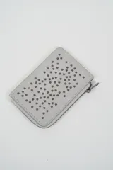 Billetera pequeña color gris claro con cierre de cremallera perimetral y tachas metálicas oscuras distribuidas en el frente.