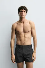 Bañador de hombre color negro, de largo medio, confeccionado en tejido técnico. Presenta cintura elástica ajustable con cordón interior, trabillas laterales, bolsillos frontales y bolsillo trasero con cierre de cremallera.