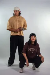 Remera color arena con cuello redondo y estampado frontal con letras "MTPE" en marrón.