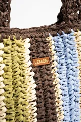 Bolso tipo shopper tejido de papel con diseño de rayas verticales en tonos marrón, celeste, verde oliva y beige. Cuenta con doble asa de hombro y detalle de etiqueta de marca en el frente.
