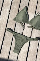 Bikini de dos piezas color marrón, con corpiño triangular fijo con corte bajo el busto, breteles regulables con hebilla y almohadillas desmontables. La bombacha es vedetina con frunce elástico en los costados.