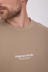 Buzo de cuello redondo y manga larga, corte relajado en color beige. Presenta el logotipo "Originals Studio" estampado en pequeño en el pecho.