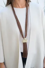 Collar largo compuesto por múltiples hilos finos de color marrón chocolate, con un dije central rectangular de metal dorado con textura irregular y un fleco largo del mismo tono que los hilos.