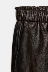 Pantalón de tiro alto confeccionado en material efecto piel, con cintura elástica ajustable mediante cordones, bolsillos delanteros y bolsillos de plastrón en la parte trasera.