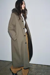 Trench reversible de corte recto con cuello de solapa y aplicación de pelo sintético extraíble. Presenta cierre frontal con botones, manga larga y bolsillos laterales ocultos en las costuras.