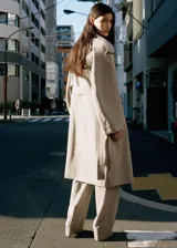 Chaqueta larga de lana 100% color gris claro, de diseño recto y doble botonadura. Cuenta con cuello de solapa con muesca, trabillas en los hombros, manga larga, dos bolsillos laterales con solapa y cinturón ajustable con hebilla. Incluye forro interior de viscosa.