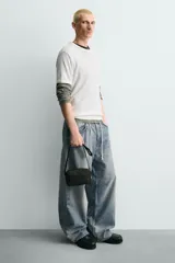 Bandolera negra con acabado engomado y textura. Cuenta con un compartimento principal con cierre de cremallera, un bolsillo plano interior y un asa de hombro ajustable y extraíble.