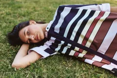 Camisa blanca de corte oversize y largo midi, confeccionada en algodón. Presenta cuello mao, cierre frontal oculto por tapeta y mangas cortas con dobladillo. Incluye un pequeño bordado de una flor en el pecho.