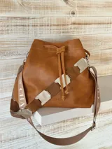 Bolso tote color marrón cuero, confeccionado en cuero genuino, con doble asa de mano y correa bandolera de tela con rayas beige y marrón.