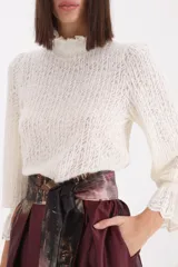 Sweater de punto calado en color crudo, con cuello alto tipo polera y mangas largas con puños con volados.