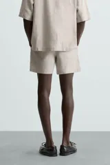 Bermuda de corte relajado color beige claro, confeccionada en lino. Presenta cintura elástica con cordón ajustable y bolsillos laterales y traseros.