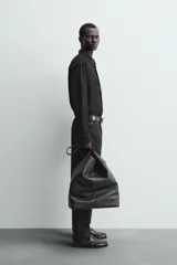 Sobrecamisa de corte regular confeccionada en piel con acabado de ante. Presenta cuello solapa, cierre frontal con botones, manga larga con puños abotonados y un bolsillo de parche en el pecho.