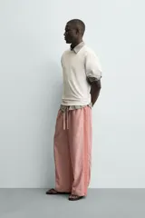Pantalón de corte relajado confeccionado en popelín de algodón, con estampado de rayas verticales blancas sobre fondo rosado. Posee cintura elástica ajustable con cordón y bandas laterales lisas en color rosado oscuro, ribeteadas con un vivo blanco.