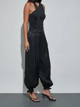 Pantalón negro de satén, de corte fluido y estilo bombacho, con cintura elástica y puños fruncidos en los tobillos con detalle de lazo.