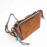 Bandolera de tamaño mediano en color marrón, confeccionada con una combinación de cuero sintético liso en los laterales y gamuza con costuras decorativas en el panel frontal. Incluye una correa ajustable y un colgante decorativo con cuentas de colores y cordón trenzado.