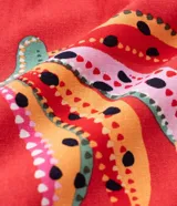 Short rojo con estampado de bananas y cocoteros, con elástico en la espalda, trabillas en la cintura, pliegues delanteros y bolsillos laterales.