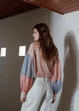 Blusa de manga larga con estampado de rayas en tonos rosados y celestes, cuello camisero, cierre frontal con botones y detalle de lazada lateral en la cintura.