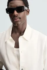 Camisa de calce relajado confeccionada en tejido ligero de lino y viscosa, con cuello solapa, manga corta y cierre frontal de botones. Presenta un diseño estampado de cactus en color gris en la parte inferior sobre un fondo blanco roto.