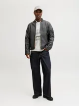 Buzo de manga larga color gris melange, con cuello tipo polo y ajuste holgado. Presenta estampado gráfico frontal con tipografía y detalles en negro, además de bandas laterales en las mangas.