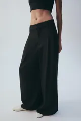Pantalón de tiro medio color marrón, con pinzas en el delantero, perneras anchas de corte recto y trabillas para cinturón. Cuenta con bolsillos laterales y traseros, y cierre frontal con cremallera y botón.
