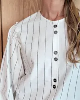 Camisa de manga larga con diseño de rayas verticales y bordados sutiles. Presenta cuello redondo, cierre frontal con botones y mangas abullonadas con volados en los hombros.