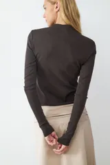 Remera de manga larga confeccionada en tejido rib, con ajuste al cuerpo y cierre frontal mediante una hilera de botones. Presenta un diseño ceñido y cuello redondo.