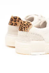 Championes de diseño moderno en tonos beige y blanco, con franja lateral de color tostado y detalle de estampado animal print en el talón. Tienen suela tipo plataforma y cierre con cordones.