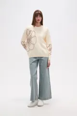 Sweater de tejido de punto color crema, con diseño holgado, cuello redondo a la base y mangas largas. Presenta apliques bordados en relieve con forma de flores en tonos rosados en el frente y las mangas.