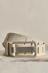 Cinturón de cuero de ancho medio color beige, con hebilla rectangular metálica envejecida y detalles de calados verticales a lo largo de toda la tira.