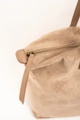 Bolso tipo shopper de gamuza vegana color tostado, con doble asa larga para hombro y cierre superior. Cuenta con una pequeña placa metálica con el logo de la marca en la parte frontal.