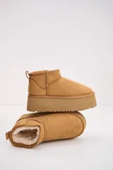 Bota corta tipo ugg en color camel, con plataforma alta y suela dentada. Presenta un diseño de gamuza con interior forrado y tirador en la parte trasera.