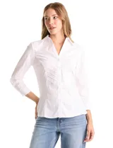 Camisa blanca de algodón con cuello camisero y escote en V. Presenta detalles plisados en el frente, cierre central con botones y mangas tres cuartos con puños abotonados. Los laterales están confeccionados en tejido modal para mayor comodidad.