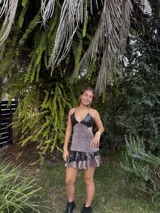 Vestido corto de tela metalizada en tono fucsia con reflejos dorados, con escote en V, diseño de top con triángulos, aberturas laterales en la cintura y doble volado irregular en el ruedo.