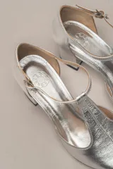 Sandalia de cuero color bordó, con acabado charolado, punta fina y tacón cuadrado de 5 cm. Presenta una tira en forma de T sobre el empeine y una correa con hebilla alrededor del tobillo.