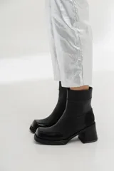 Bota corta de cuero negro con diseño bicolor que combina cuero liso y cuero charol en la puntera. Cuenta con taco cuadrado de altura media y cierre lateral interno.