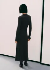 Vestido largo gris oscuro de tejido melange, con cuello perkins, manga larga y diseño entallado. Cuenta con detalle fruncido en la cintura y una anilla decorativa plateada en el lateral.