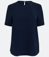 Blusa blanca de poliéster con cuello redondo, mangas cortas, cierre trasero en forma de gota, pequeñas aberturas laterales y acabados en pespuntes en las mangas y el cuello.