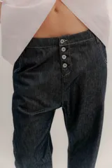 Pantalón de denim oscuro con tiro bajo y calce relajado. Presenta un cierre frontal con botones a la vista y costuras en contraste.