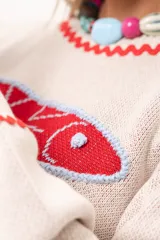 Sweater tejido color crudo con cuello redondo y mangas largas. Presenta dos peces rojos con detalles en azul bordados en el frente. Tiene ribete ondulado rojo en cuello, puños y ruedo.