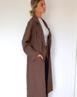 Trench largo de color marrón, con solapas amplias, cierre frontal de doble botonadura y bolsillos laterales.