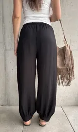 Pantalón negro tipo babucha con cintura elástica fruncida y cordón ajustable, corte holgado y puños elásticos en los tobillos.