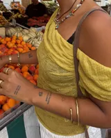 Collar corto de estilo artesanal, compuesto por una variedad de piedras naturales en tonos tierra, verdes, rojos y amarillos, intercaladas con pequeñas perlas de río. Presenta dijes de bronce macizo con formas orgánicas, incluyendo una figura de pez y un dije circular central, unidos por un cierre de barra y argolla.