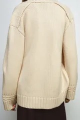 Chaqueta cruzada de punto color beige con manga larga, cuello smoking y cierre frontal con lazada. Presenta detalles de calados en los puños.