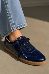 Championes de cuero vacuno con acabado brillante tipo charol, color azul marino, con cordones al tono y suela de goma color caramelo.