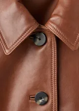 Chaqueta de cuero ovino color marrón, con diseño corto, cuello camisero, cierre frontal con botones y puños elásticos.