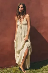 Vestido largo color crudo de tela satinada, con escote en V, tirantes finos ajustables, detalle de cordón ajustable en el pecho y diseño fruncido en capas.