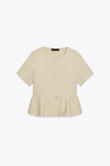 Chaqueta de punto color beige claro, con cuello redondo, manga corta y bajo peplum con pliegues. Cierre frontal con botones forrados a tono.