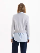 Sweater de tejido de punto en color gris, con cuello redondo, mangas largas y detalle de bordado amarillo en el puño y en el lateral inferior. Presenta un corte recto y estructura ligera.