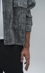 Campera de denim rígido con diseño de trama texturizada en tonos grises y negros. Presenta cuello camisero, cierre frontal con botones, mangas largas y dos bolsillos frontales con solapa.